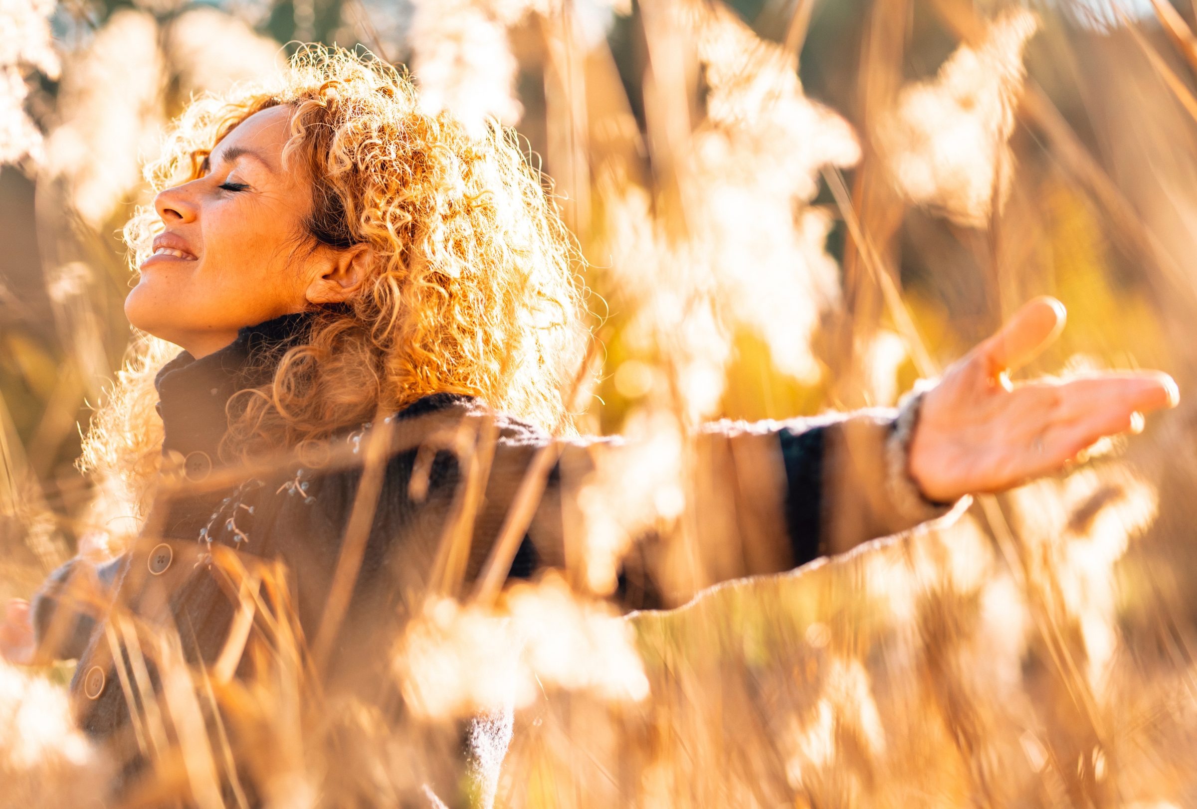 Woman standing in a golden field with her arms open